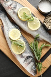 Photo of Fresh raw seabass with spices on black table, top view. Fish and seafood delicacies