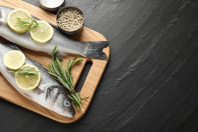 Photo of Fresh raw seabass fish with spices on black table, top view and space for text. Seafood delicacies