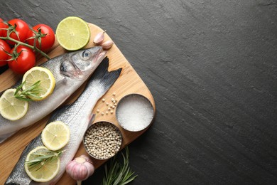 Photo of Fresh raw seabass fish with spices on black table, top view and space for text. Seafood delicacies