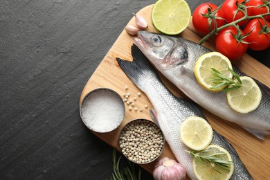 Photo of Fresh raw seabass fish with spices on black table, top view and space for text. Seafood delicacies
