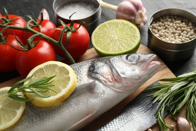 Photo of Fresh raw seabass with spices on black table, closeup. Fish and seafood delicacies