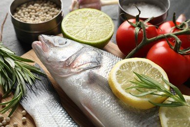 Photo of Fresh raw seabass with spices on black table, closeup. Fish and seafood delicacies