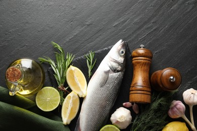 Photo of Fresh raw seabass fish with spices on black table, flat lay and space for text. Seafood delicacies