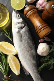 Photo of Fresh raw seabass with spices on black table, flat lay. Fish and seafood delicacies