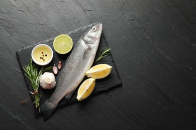 Photo of Fresh raw seabass fish with spices on black table, top view and space for text. Seafood delicacies