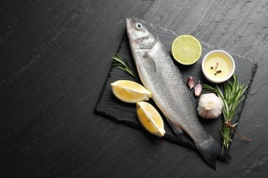 Photo of Fresh raw seabass fish with spices on black table, top view and space for text. Seafood delicacies