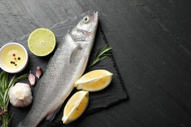 Photo of Fresh raw seabass fish with spices on black table, top view and space for text. Seafood delicacies