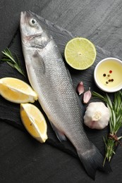 Photo of Fresh raw seabass with spices on black table, top view. Fish and seafood delicacies