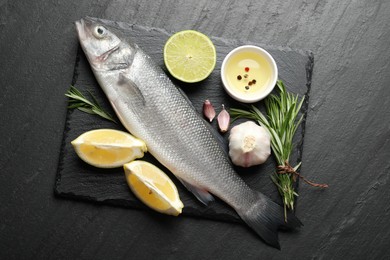 Photo of Fresh raw seabass with spices on black table, top view. Fish and seafood delicacies