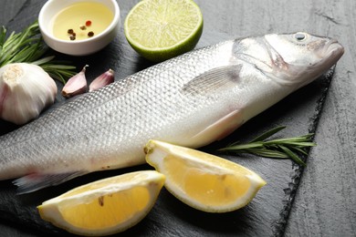 Photo of Fresh raw seabass with spices on black table, closeup. Fish and seafood delicacies