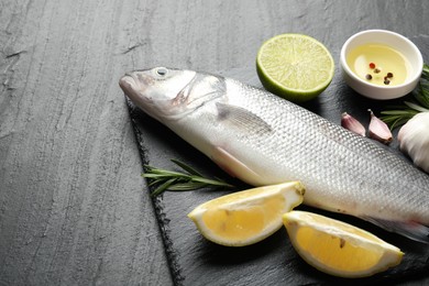 Photo of Fresh raw seabass with spices on black table, closeup. Fish and seafood delicacies