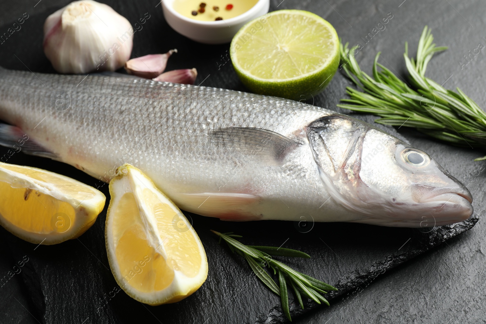 Fresh raw seabass with spices on black table, closeup. Fish and seafood delicacies Photo of Fresh raw seabass with spices on black table, closeup. Fish and seafood delicacies