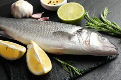 Photo of Fresh raw seabass with spices on black table, closeup. Fish and seafood delicacies