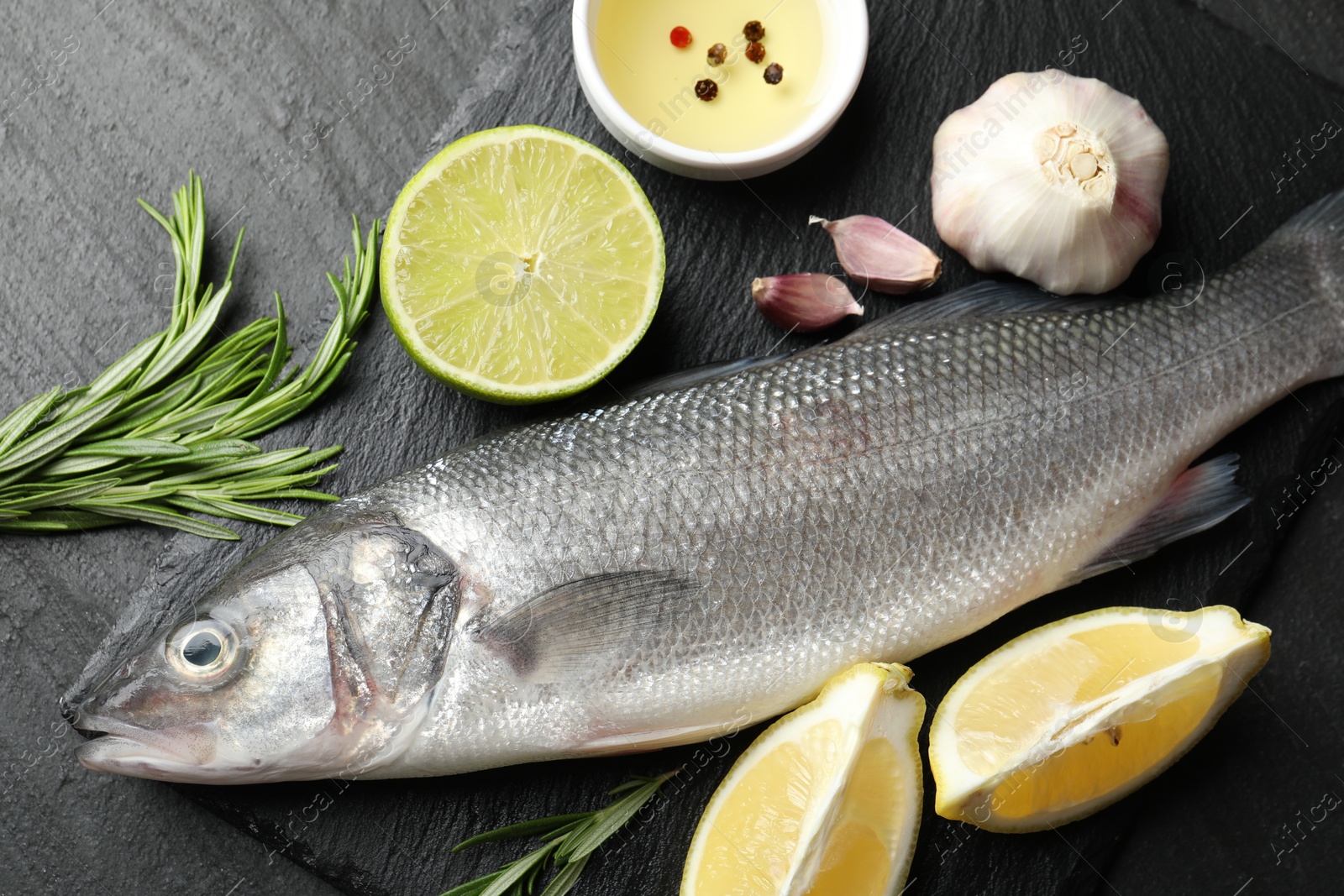 Fresh raw seabass with spices on black table, flat lay. Fish and seafood delicacies Photo of Fresh raw seabass with spices on black table, flat lay. Fish and seafood delicacies