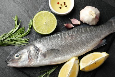 Photo of Fresh raw seabass with spices on black table, flat lay. Fish and seafood delicacies