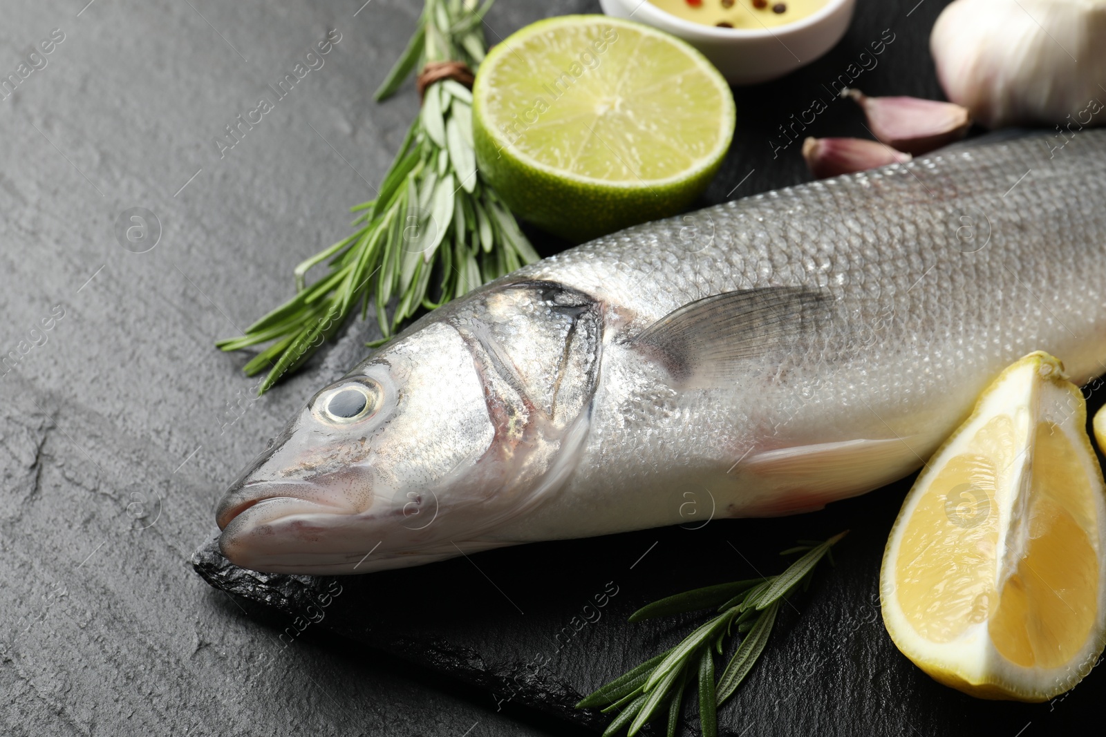 Fresh raw seabass with spices on black table, closeup. Fish and seafood delicacies Photo of Fresh raw seabass with spices on black table, closeup. Fish and seafood delicacies