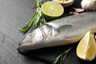 Photo of Fresh raw seabass with spices on black table, closeup. Fish and seafood delicacies