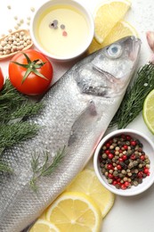 Photo of Fresh raw seabass with spices on white table, flat lay. Fish and seafood delicacies