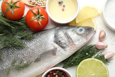 Photo of Fresh raw seabass with spices on white table, flat lay. Fish and seafood delicacies
