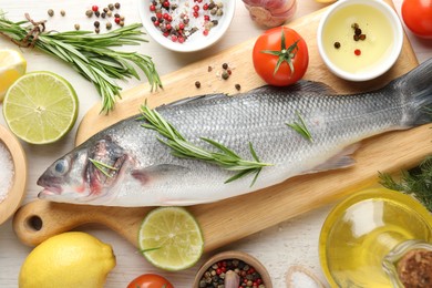 Photo of Fresh raw seabass with spices on white wooden table, flat lay. Fish and seafood delicacies