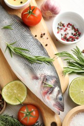 Photo of Fresh raw seabass with spices on white wooden table, flat lay. Fish and seafood delicacies