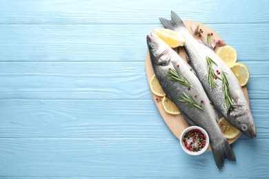 Photo of Fresh raw seabass fish with spices on blue wooden table, top view and space for text. Seafood delicacies