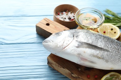Photo of Fresh raw dourade fish with spices on blue wooden table, closeup and space for text. Seafood delicacies