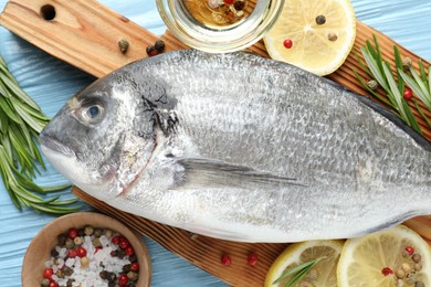 Photo of Fresh raw dourade with spices on blue wooden table, closeup. Fish and seafood delicacies