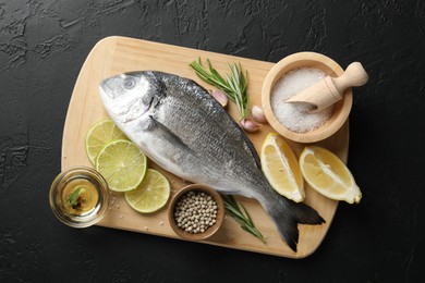 Photo of Fresh raw dourade with spices on black table, top view. Fish and seafood delicacies