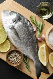 Photo of Fresh raw dourade with spices on black table, top view. Fish and seafood delicacies