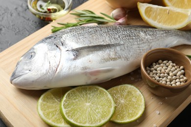 Photo of Fresh raw dourade with spices on black table, closeup. Fish and seafood delicacies