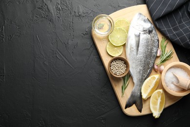 Photo of Fresh raw dourade fish with spices on black table, top view and space for text. Seafood delicacies
