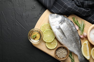 Photo of Fresh raw dourade fish with spices on black table, top view and space for text. Seafood delicacies