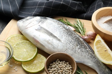 Photo of Fresh raw dourade with spices on black table, closeup. Fish and seafood delicacies