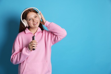 Photo of Smiling teenage girl in headphones with smartphone on light blue background. Space for text