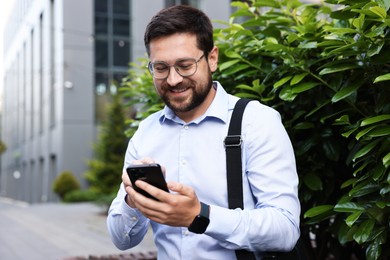 Photo of Successful businessman with smartphone near office building
