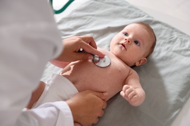 Photo of Pediatrician examining baby with stethoscope at table in clinic, closeup