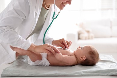 Photo of Pediatrician examining baby with stethoscope at table in clinic, closeup