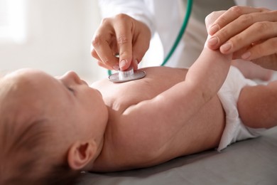 Photo of Pediatrician examining baby with stethoscope at table in clinic, closeup