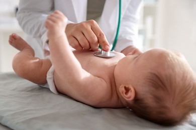 Photo of Pediatrician examining baby with stethoscope at table in clinic, closeup