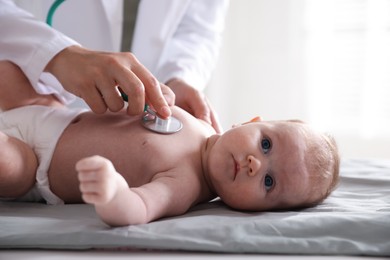 Photo of Pediatrician examining baby with stethoscope at table in clinic, closeup