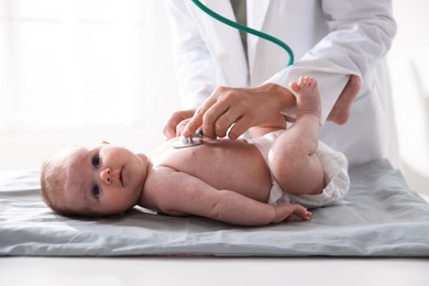 Photo of Pediatrician examining baby with stethoscope at table in clinic, closeup