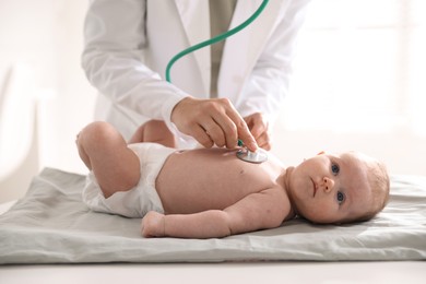 Photo of Pediatrician examining baby with stethoscope at table in clinic, closeup