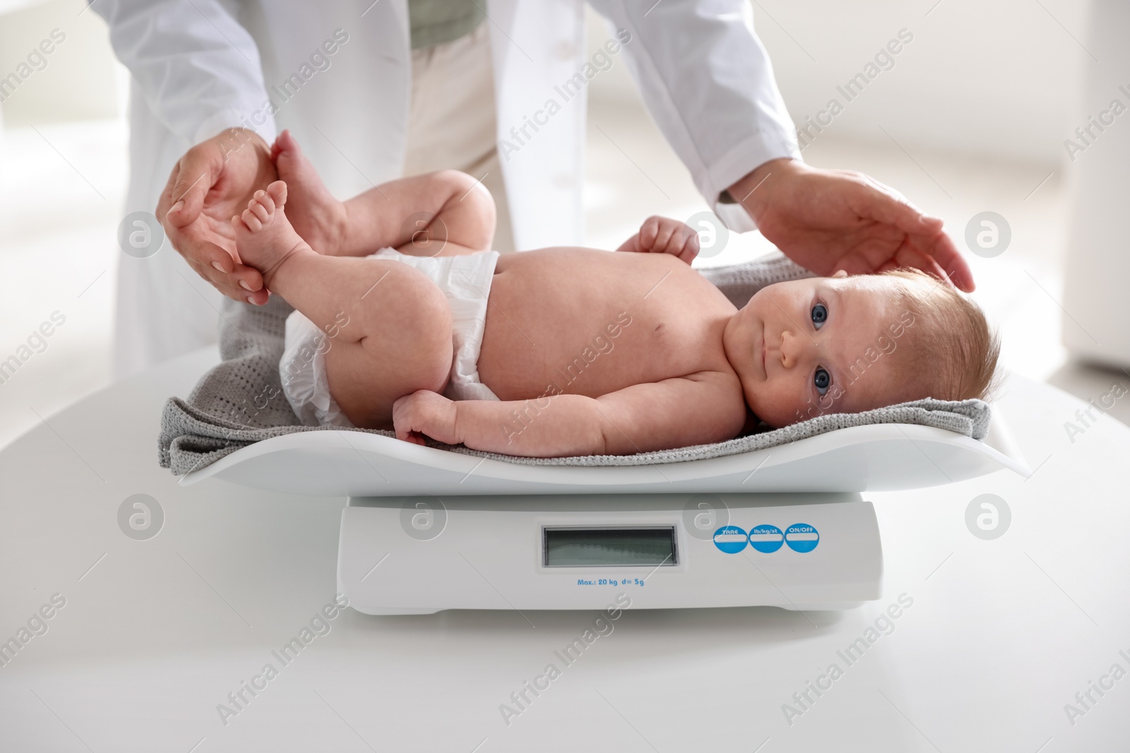 Pediatrician weighting baby with scales at white table in clinic, closeup Photo of Pediatrician weighting baby with scales at white table in clinic, closeup