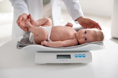Photo of Pediatrician weighting baby with scales at white table in clinic, closeup