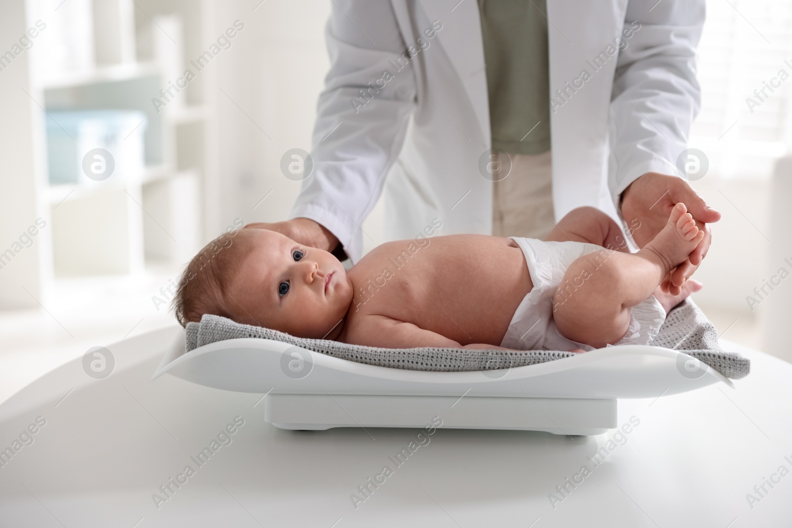 Pediatrician weighting baby with scales at white table in clinic, closeup Photo of Pediatrician weighting baby with scales at white table in clinic, closeup