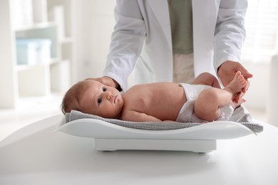 Photo of Pediatrician weighting baby with scales at white table in clinic, closeup
