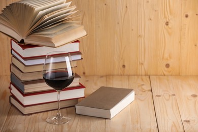 Photo of Glass of red wine and stacked books on wooden table. Space for text