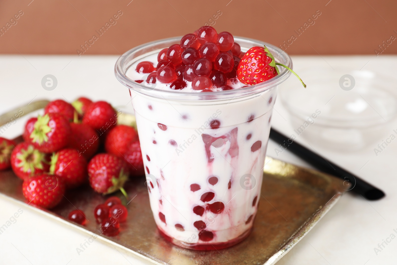 Photo of Tasty milk bubble tea in plastic cup and strawberries on white table, closeup