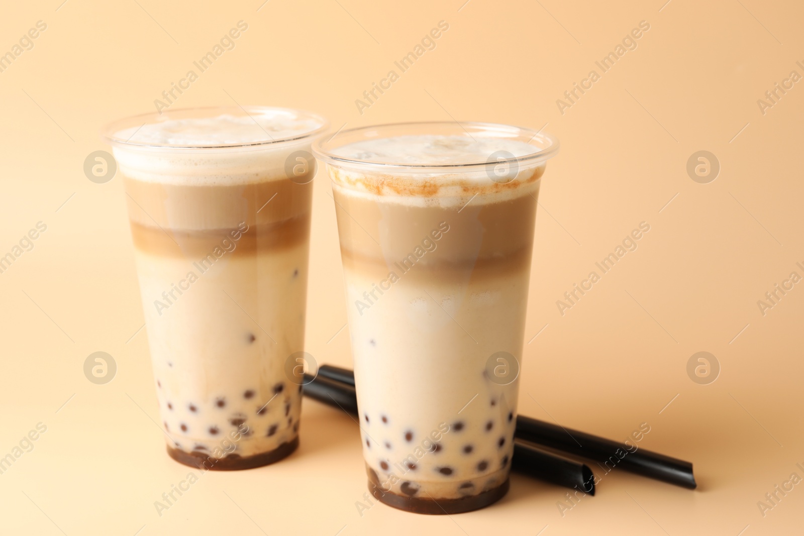 Tasty milk bubble tea in plastic cups on beige background, closeup Photo of Tasty milk bubble tea in plastic cups on beige background, closeup